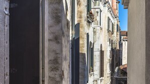 A narrow street with historic buildings, including a building with a large black door and a building with a pink chimney. - ACQUARELLO, SPACIOUS APARTMENT IN THE HEART OF VENICE (Venise)