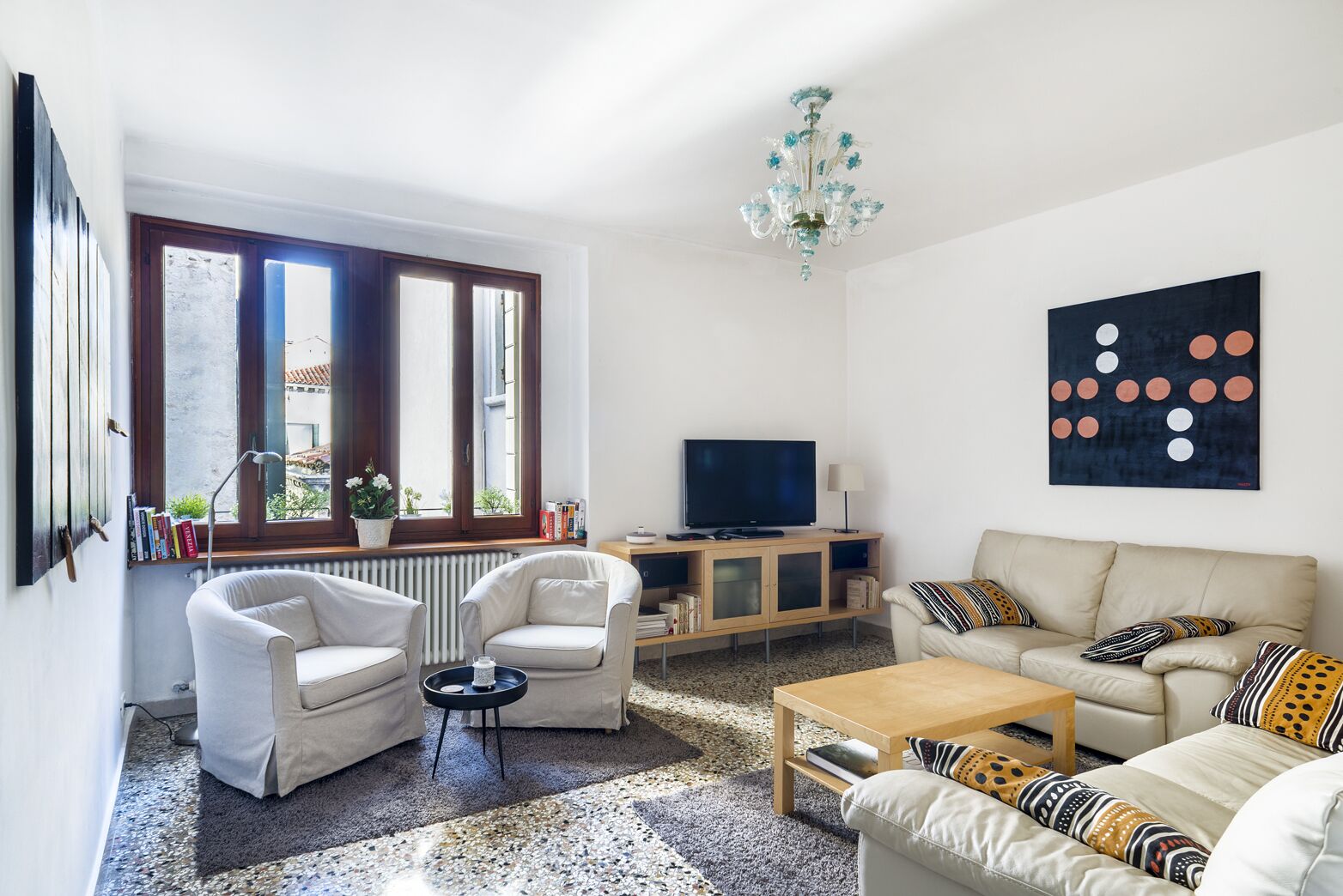 A modern living room with a sofa, armchairs, a coffee table, a TV, and a bookshelf.