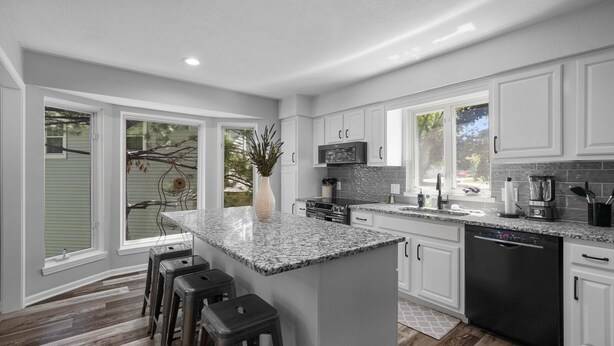 A modern kitchen with white cabinets, a granite countertop, and a central island with bar stools. - KC Backyard Vacation (Kansas City)