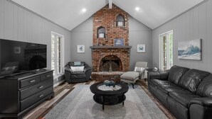 A modern living room with a brick fireplace, leather sofas, a flat-screen TV, and a coffee table. - KC Backyard Vacation (Kansas City)