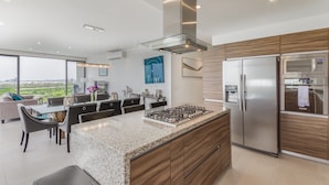 A modern kitchen with a central island, stainless steel appliances, and a dining area with a view. - Apartment (Zapopan)