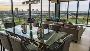 A modern dining area with a glass table, chairs, and a view of a cityscape through large windows. - Apartment (Zapopan)