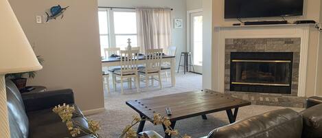 A living room with a fireplace, a television, a dining area with chairs, and a ceiling fan.