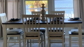 A dining area with a table and four chairs, a decorative vase, and a view of the ocean through large windows. - Reel Em Inn Bay Front House With boat ramp (port saint joe/simmons bayou)