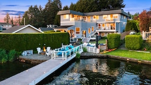 A two-story house with a dock extending into a canal. There are outdoor seating areas and a small boat docked on the dock. - Relaxing 4 bed, 4 bath, + private studio lakefront home on Lake Stevens! (Lake Stevens)
