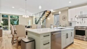 A modern kitchen with a central island, stainless steel appliances, and a dining area with a staircase. - Luxury Alki Beach Townhome w/ Large Private Rooftop & Amazing Views! (Seattle)