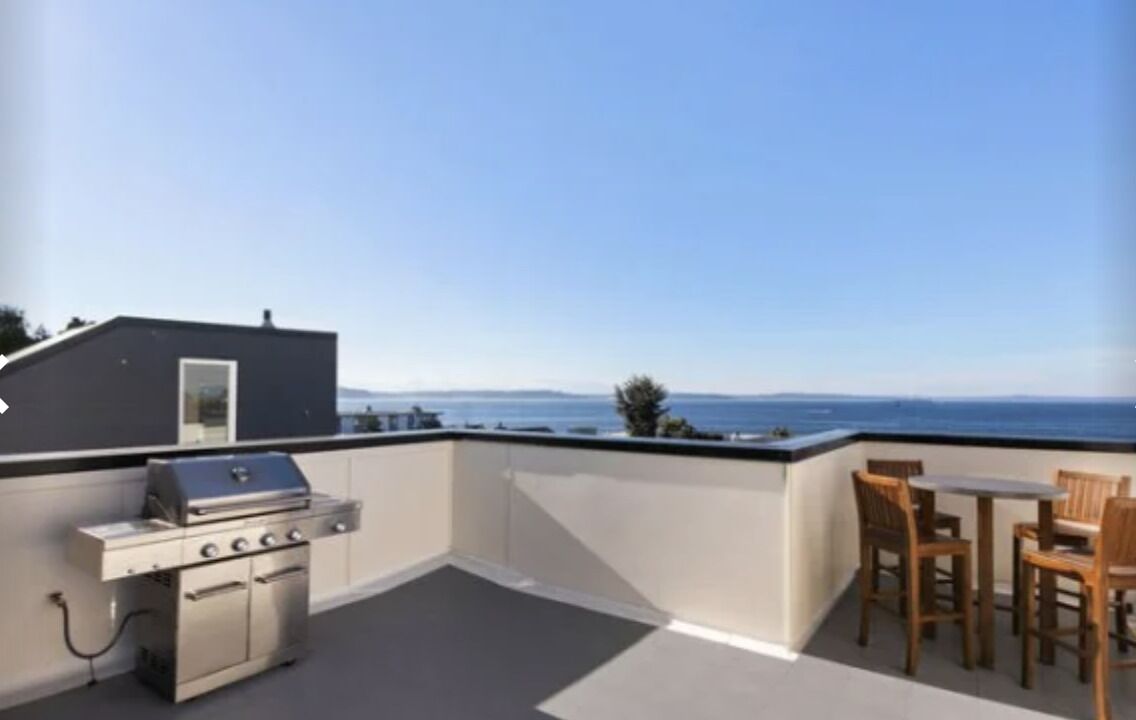 A rooftop terrace with a grill and wooden chairs.