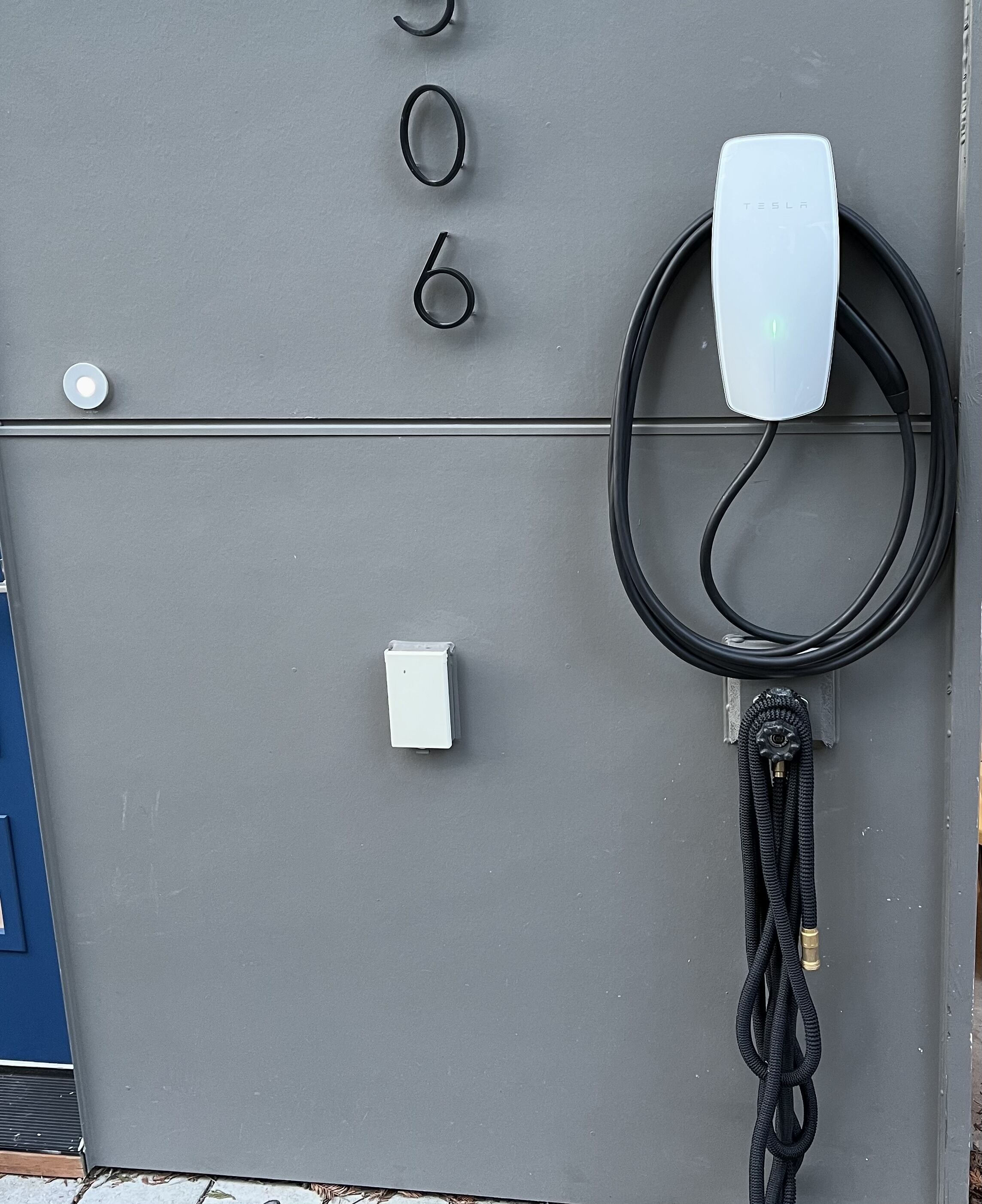 A Tesla charging station with a cable connected to a vehicle, a power outlet, and a control panel.