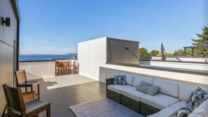 A modern outdoor seating area with a white sofa and chairs, overlooking a scenic view. - Luxury Alki Beach Townhome w/ Large Private Rooftop & Amazing Views! (Seattle)