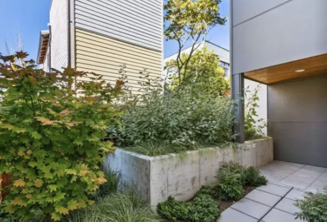 Un bâtiment moderne doté d’un jardinier en béton rempli de différentes plantes.