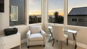 A modern room with a large window, a white sofa, a glass table, and a printer on a cabinet. - Luxury Alki Beach Townhome w/ Large Private Rooftop & Amazing Views! (Seattle)