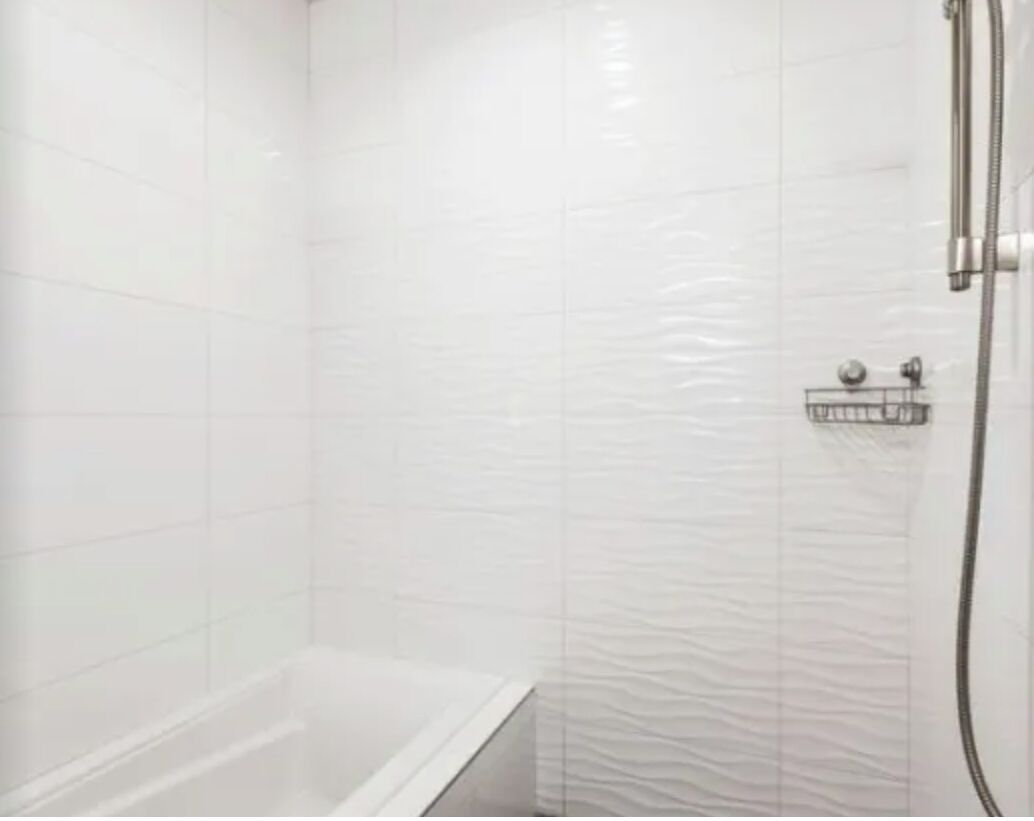 A bathroom with white tiled walls and a shower area.