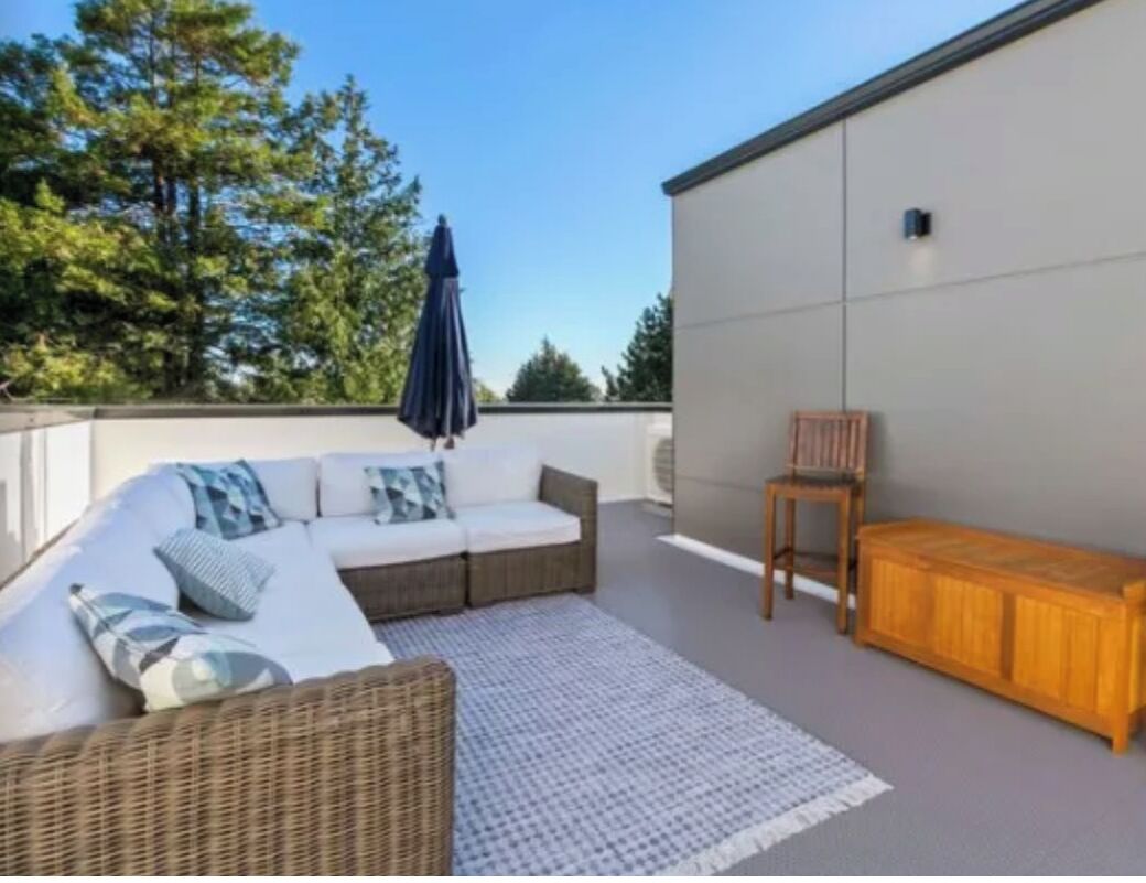 Un patio en la azotea con un sofá de mimbre, un banco de madera y un tapiz estampado.