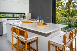 Une cuisine moderne dotée d’un grand îlot central, de tabourets de bar et offrant une vue sur la verdure environnante.