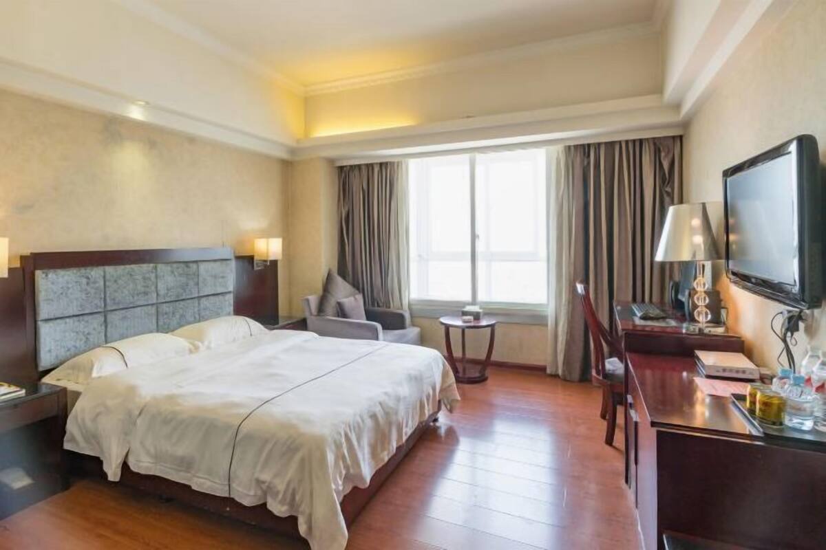 A hotel room with a large bed, a desk with a chair, a television, and a window with curtains.