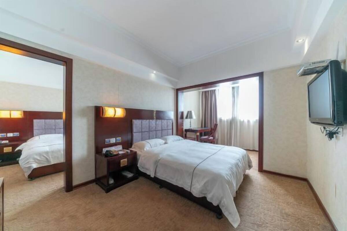 A hotel room with a large bed, a desk, a chair, a TV, and a mirror.