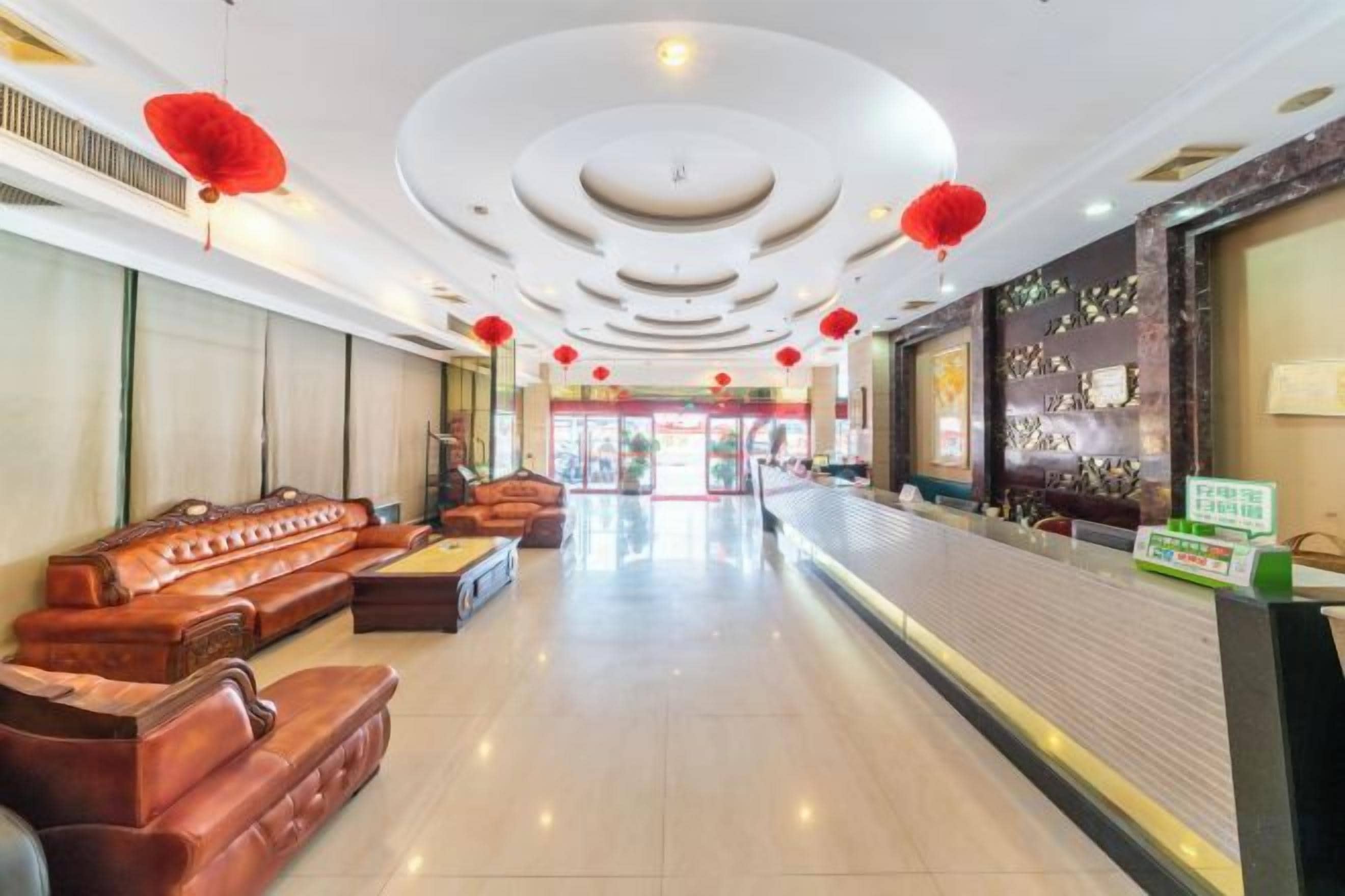Un hall d’hôtel comprenant un comptoir d’accueil, un espace salon avec des fauteuils en cuir et un plafond décoratif.
