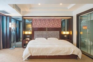 Habitación de hotel con una cama grande, lámparas de noche, una mesita de noche y un ventanal de cristal que da a un balcón.