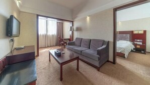 Habitación de hotel con sofá, mesa de centro, televisor, cama y escritorio.