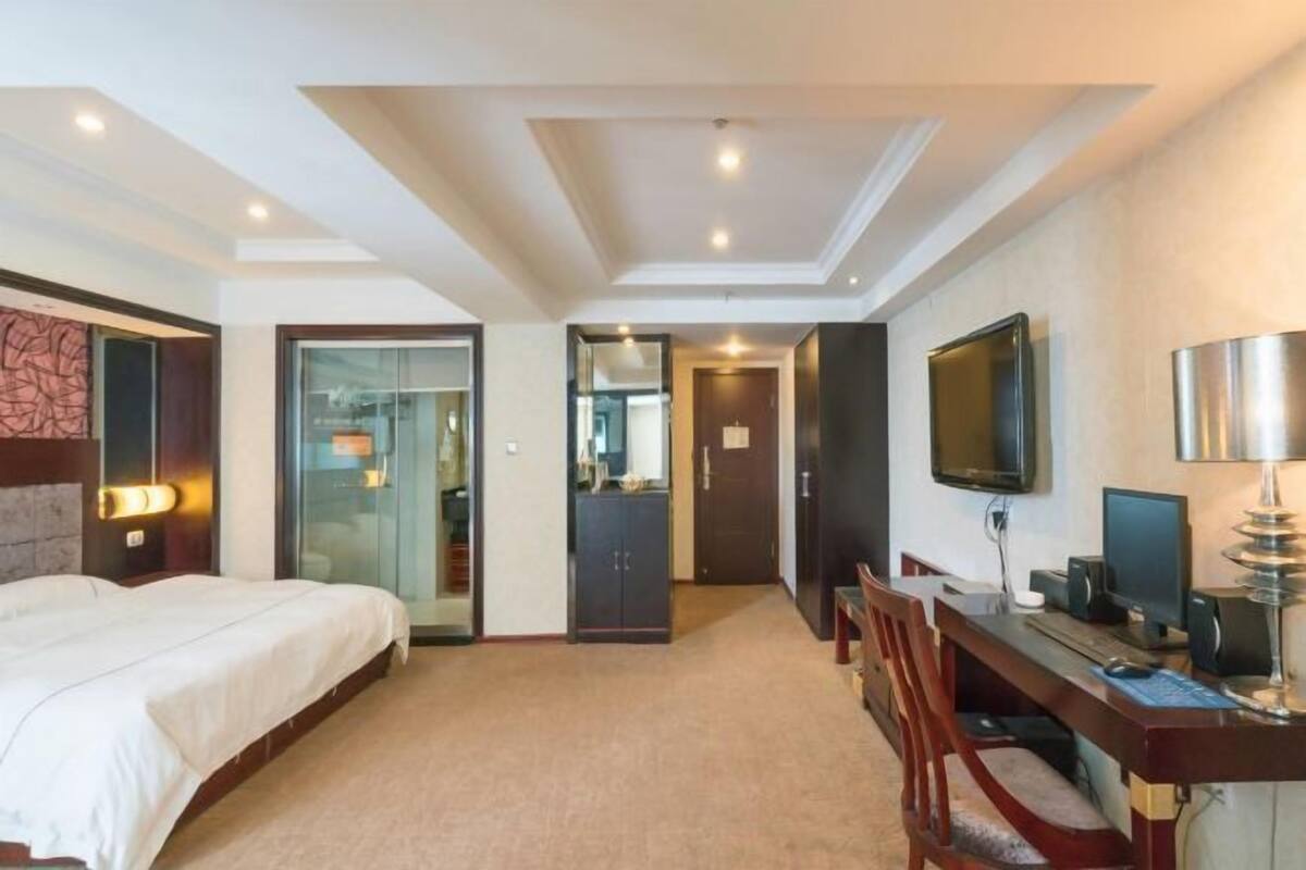 A hotel room with a bed, desk, computer, TV, and a door leading to a bathroom.