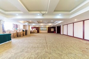 A large hall with a patterned carpet, a stage with chairs, and a projection screen.