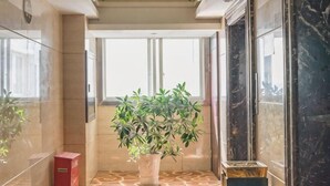 A hallway with a potted plant, a red trash bin, and a marble floor. - Ling Nan International Hotel (Xing'an County)