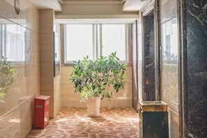A hallway with a potted plant, a red trash bin, and a marble floor. - Ling Nan International Hotel (Xing'an County)