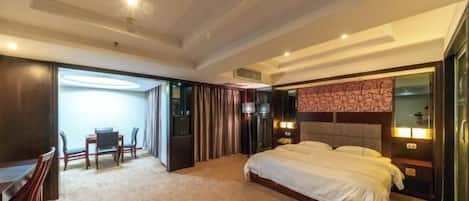 A hotel room with a large bed, a desk with chairs, a TV, and a minibar.