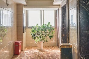 A hallway with a potted plant, a red trash bin, and a marble floor. - Ling Nan International Hotel (Xing'an County)