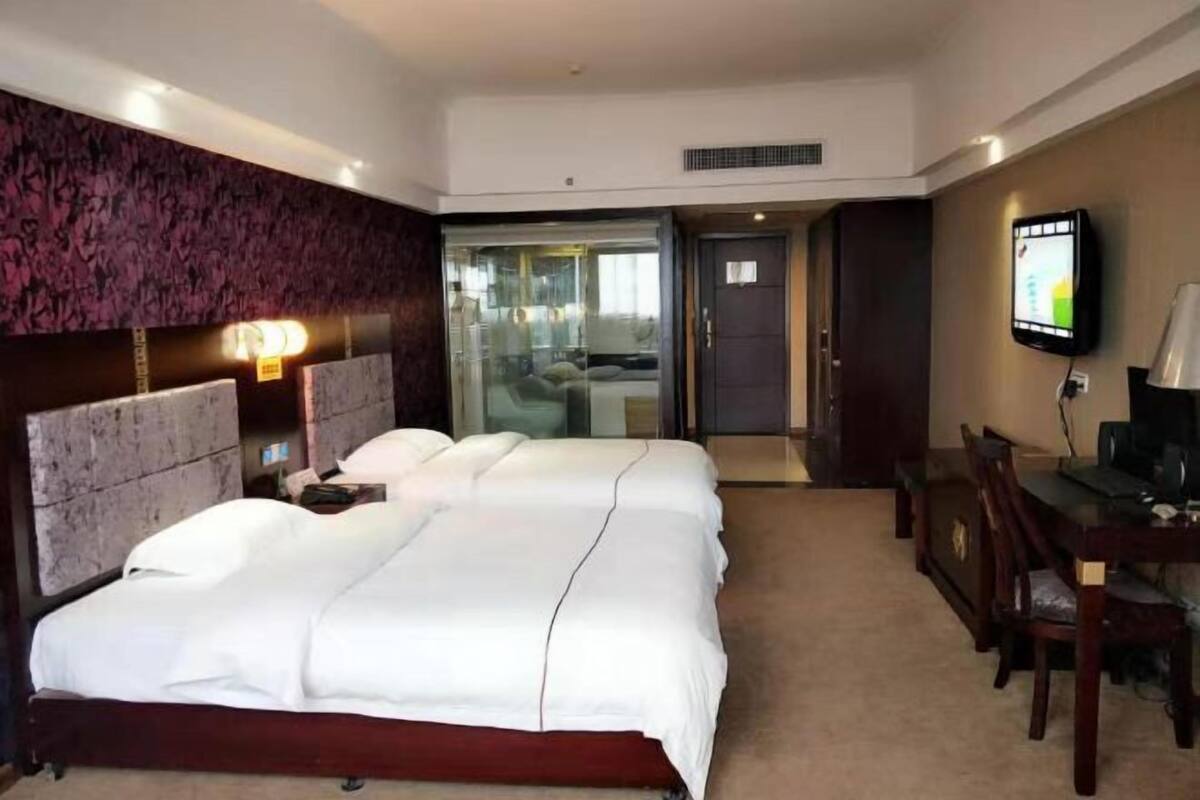 A hotel room with a large bed, a desk, a television, and a sliding door leading to a balcony.