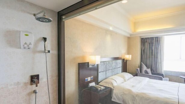 Una habitación de hotel con cama, lámparas de noche, mesita de noche, ducha y ventana con cortinas.