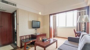 Habitación de hotel con sofá, televisión, escritorio y ventana con cortinas.