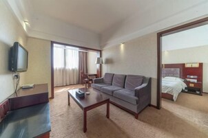 Una habitación de hotel con sofá, mesa de centro, televisor, cama y escritorio.
