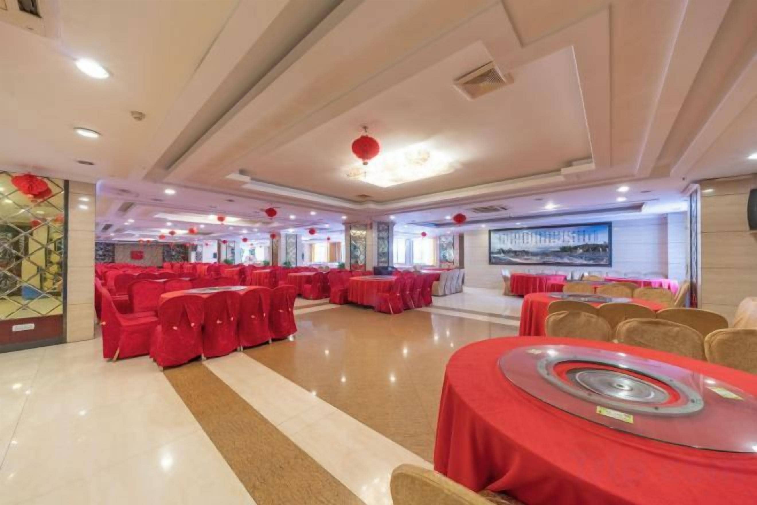 A banquet hall with round tables covered in red tablecloths, arranged in rows.