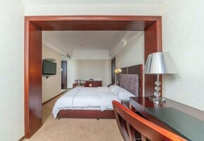 Quarto de hotel com cama, mesa de cabeceira, luminária e escrivaninha.