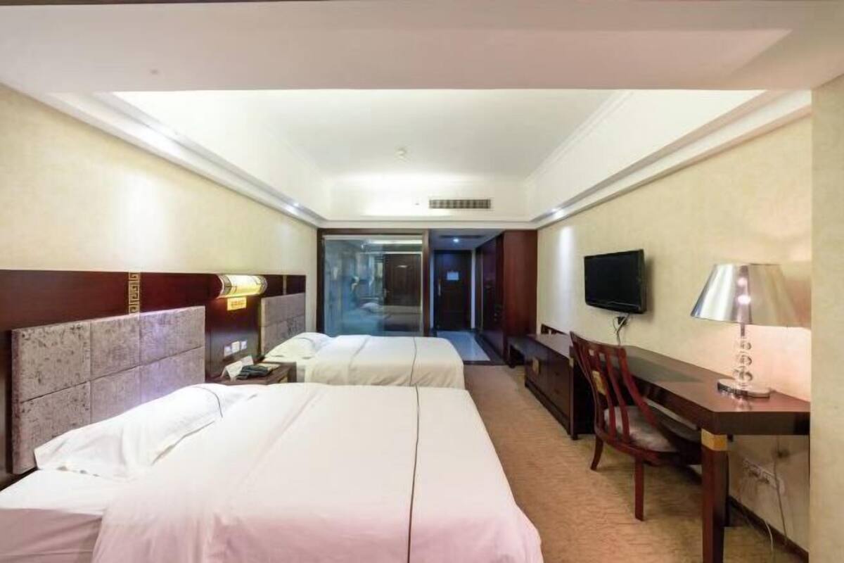 A hotel room with two beds, a desk, a chair, a TV, and a sliding door leading to a bathroom.