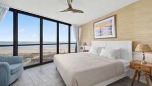 A bedroom with a large window overlooking a beach, a bed, a chair, and a bedside table with a lamp. - 2 Bdrm Oceanfront-Pool, Xbox, Pickleball, Gym, HBO (Ocean City)