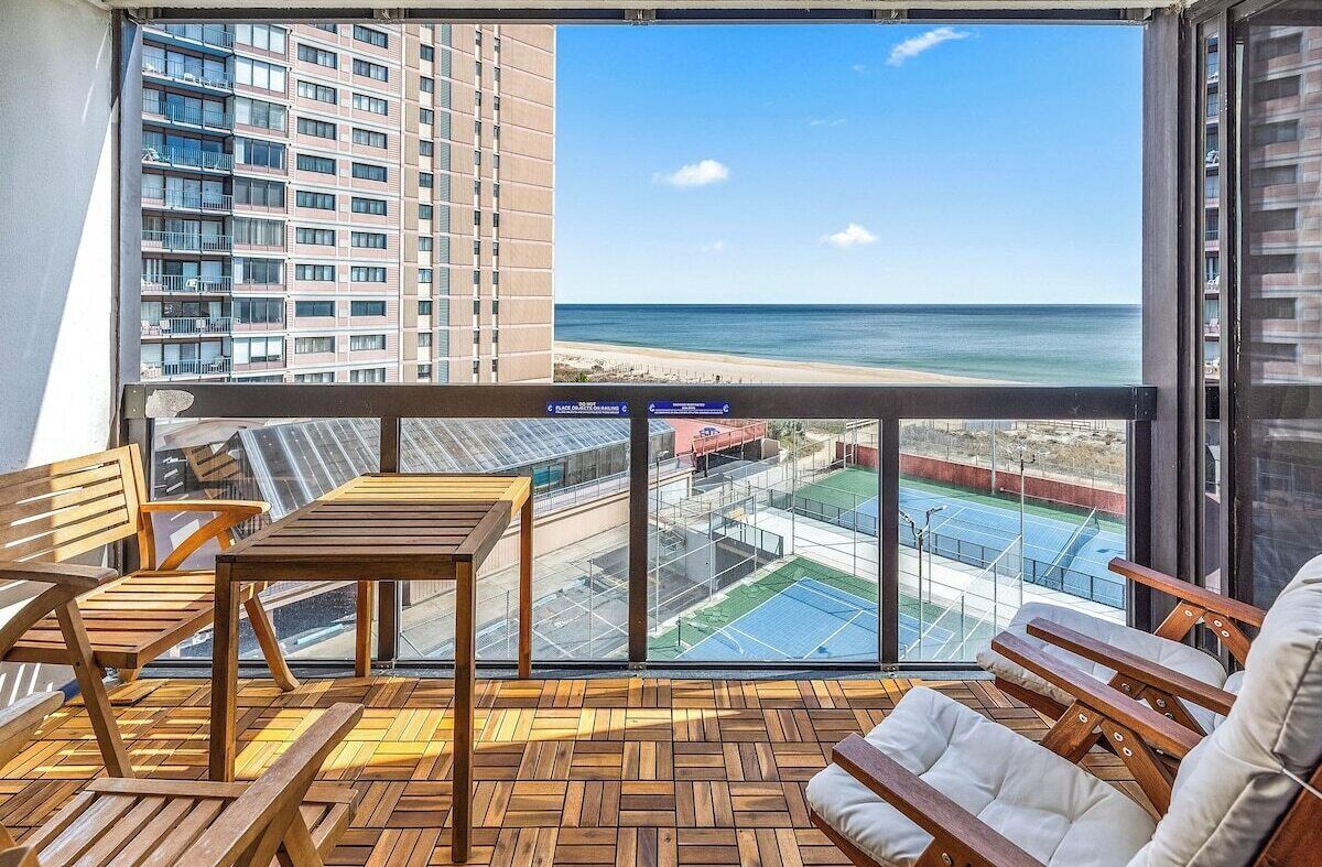 Un balcon avec des meubles en bois, une vue sur la plage et un court de tennis.