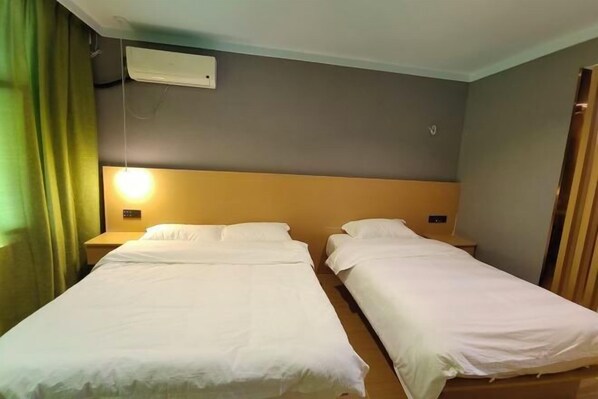A hotel room with two single beds, a bedside table with a lamp, and a wall-mounted air conditioner. - Fangcao Business Hotel (New Barag Right Banner)