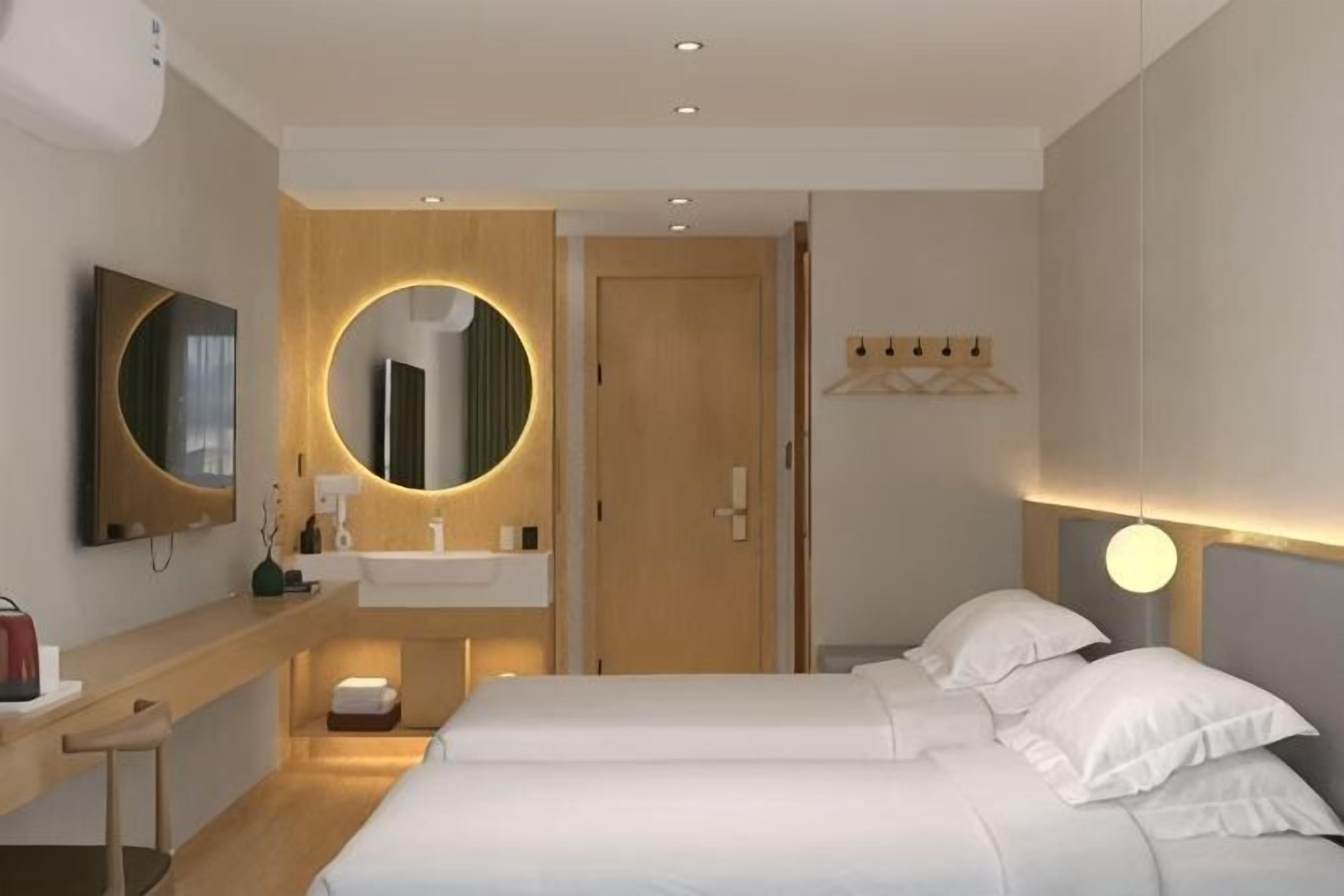 A hotel room with a bed, bedside table, mirror, and a wall-mounted TV.