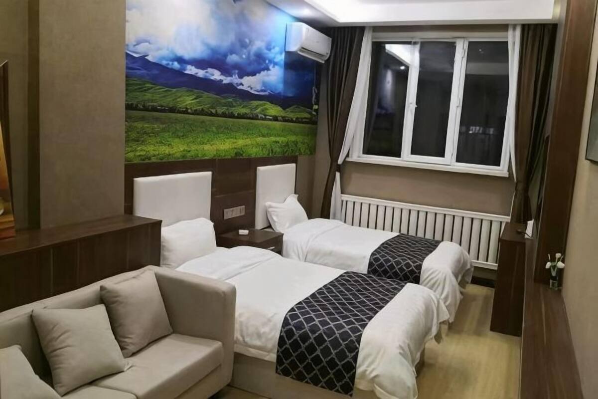 Hotellihuone, jossa on kaksi sänkyä, sohva, suuri ikkuna ja seinämaalaus, jossa on kuvattuna maisema.