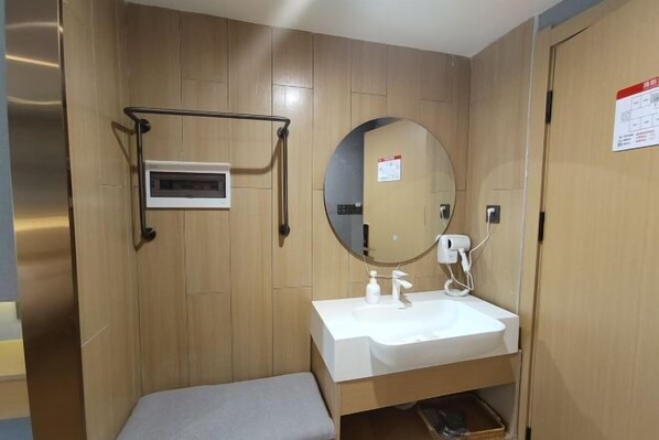 Un baño pequeño con pared de madera, un lavamanos blanco, un espejo redondo y un estante pequeño.