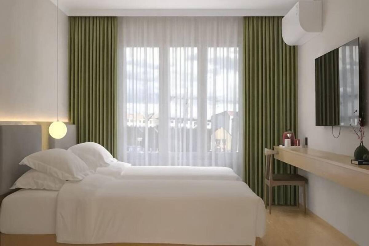 Hotellihuone, jossa on sänky, työpöytä, tuoli ja ikkuna, jossa on verhot.