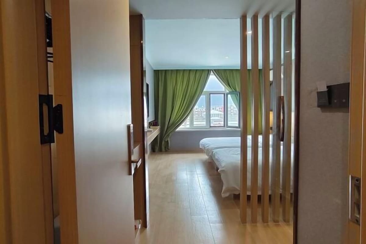 Una habitación de hotel con cama, escritorio, ventana con cortinas y vistas a edificios.