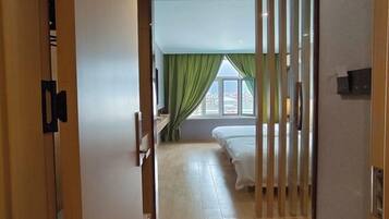 Una habitación de hotel con cama, escritorio, ventana con cortinas y vistas a edificios.