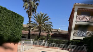 A rectangular swimming pool with clear blue water, surrounded by a white fence and palm trees. - Apartment near center 5 min walk and 5 min drive to beaches (La Croix-Valmer)