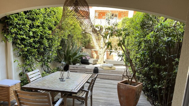 A wooden deck with a table and chairs, surrounded by lush greenery and a pergola. - Apartment near center 5 min walk and 5 min drive to beaches (La Croix-Valmer)
