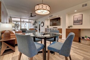 Een moderne eetruimte met een tafel met glazen blad, blauwe bekleden stoelen en een hanglamp.
