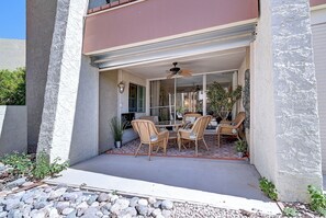 Une terrasse extérieure dotée d’une porte vitrée, de meubles en osier et d’un ventilateur de plafond.