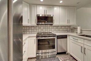 Une cuisine moderne avec des meubles blancs, une cuisinière en acier inoxydable, un four encastré et un lave-vaisselle.